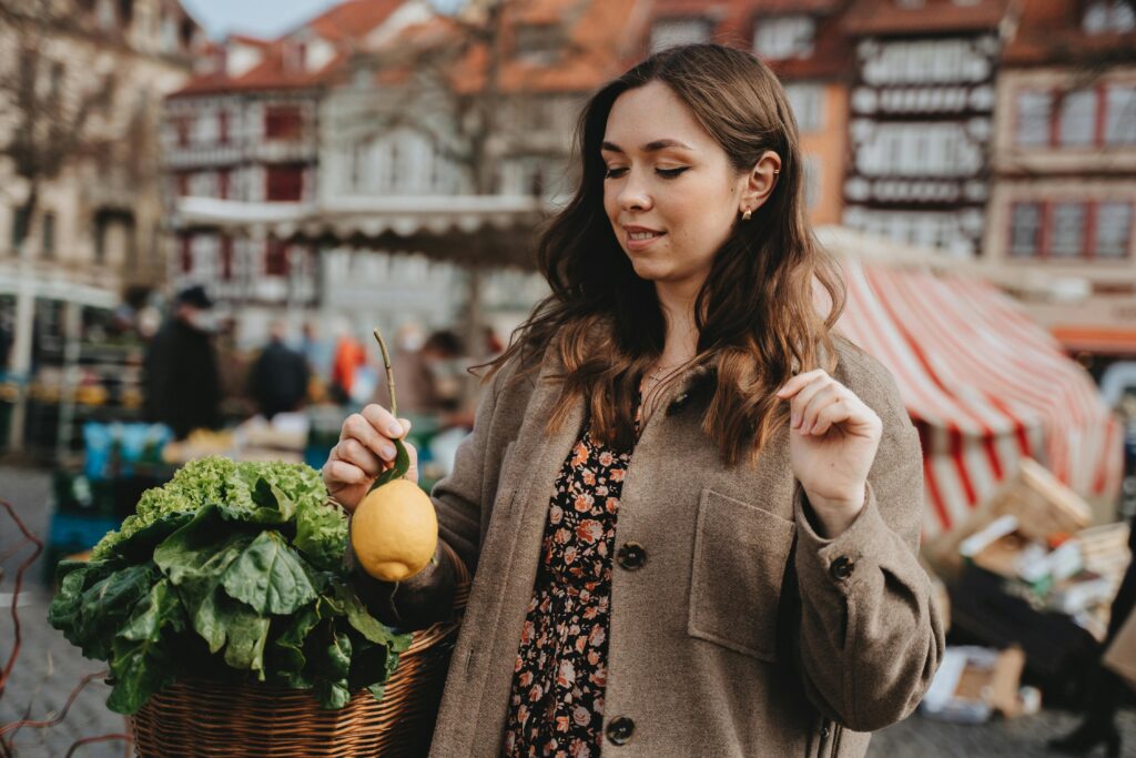 Young woman exploring Erfurt's vibrant farmers market, holding fresh produce in a bustling outdoor setting.