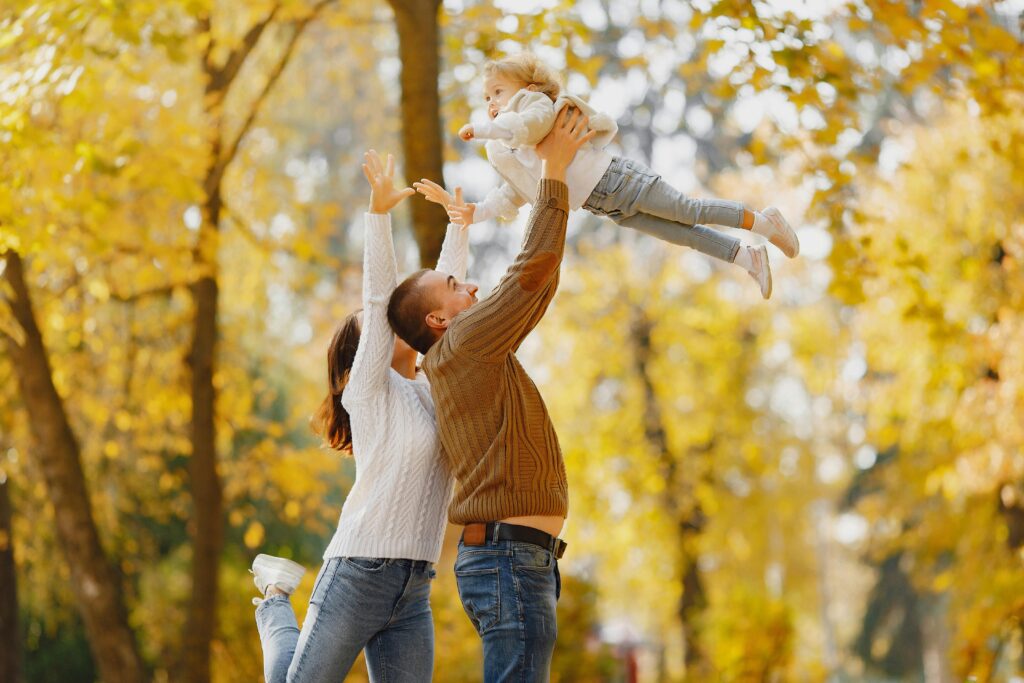 Side view of happy young parents standing close to each other while playing with cute little daughter throwing up and catching child with raised arms